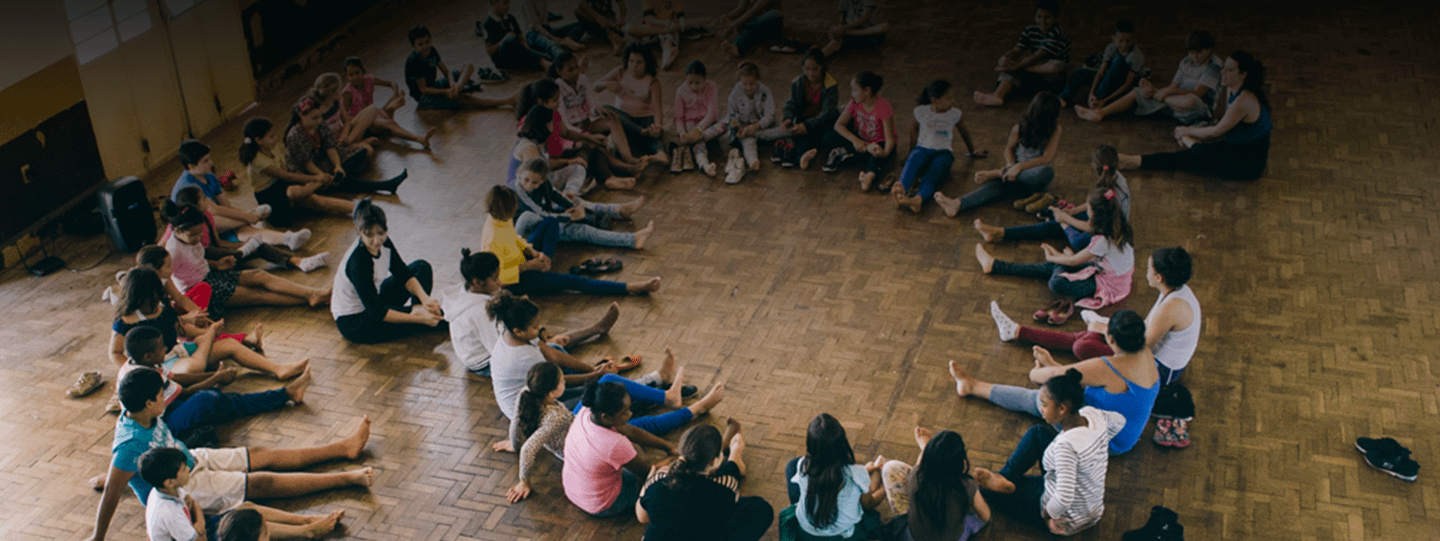 Children and teenagers sitting in a circle, barefoot. Some of them are doing a foot massage, with their hands.