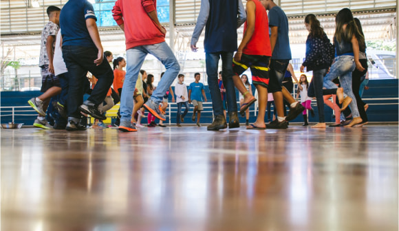 Foto colorida com foco nos pés de crianças e adolescentes formando uma roda de dança.